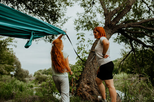 Hammock hanging on tree, mother and daughter nearby