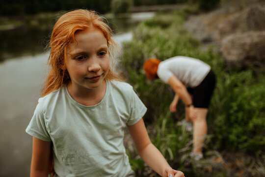 Portrait of redhead girl by lake, mother in background