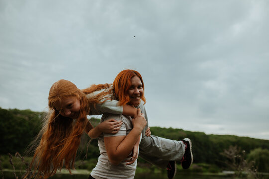 Mother and daughter hugging and laughing against sky