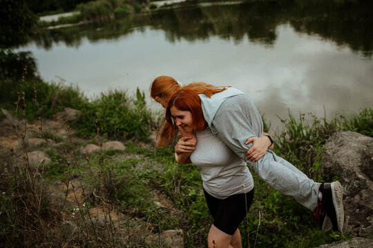Mother giving daughter piggyback ride by lake