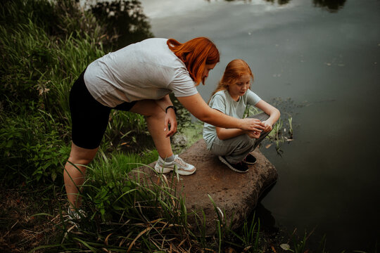 Mother and daughter releasing frog into lake from rock