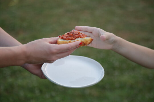 Close-up of woman handing slice of bread with ajvar to child, homemade food, family sharing moment outdoors