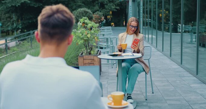 Professional businesswoman on an outdoor cafe near a modern office building, using smartphone while drinking coffee during her lunch break on the terrace of a modern office. Professional manager