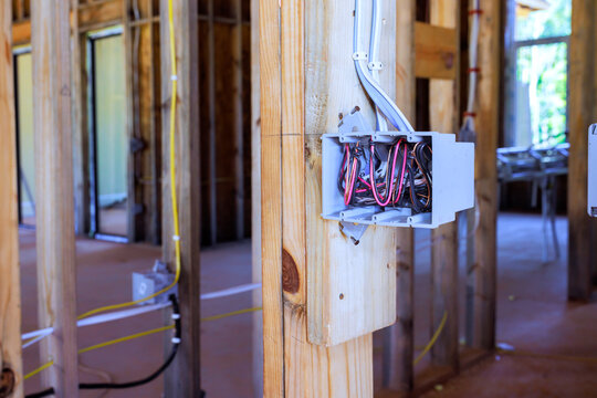 An open junction box with exposed wires is mounted on timber stud wall inside building under construction.