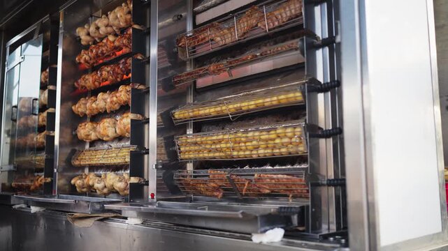Whole chickens slowly roasting on a rotating rotisserie spit at an outdoor food stall. Street food preparation, freshly roasted meat, outdoor cooking, takeaway meals, and food vendor business