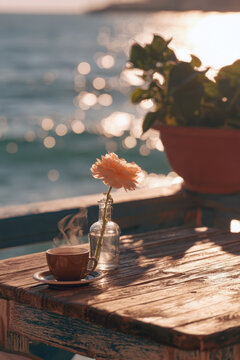 steaming cup of coffee and pink flower in glass vase on rustic wooden table over sparkling sea background at sunset cozy morning mood peaceful seaside cafe terrace scenic romantic view wallpaper
