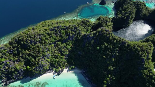 Aerial view of Coron Island with lush green limestone cliffs, turquoise waters, and a small sandy beach in Coron, Mimaropa, Philippines.