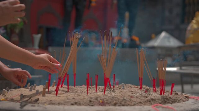 female hands placing burning incense sticks into sand burner, person holding smoking spiritual offering at buddhist temple 4k