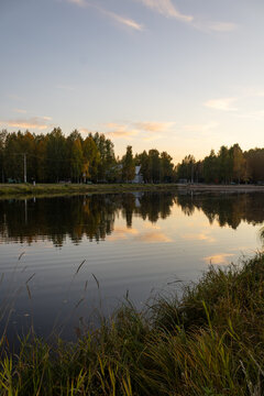 Vertical landscape of a calm autumn pond reflecting colorful trees and sunset clouds at dusk in a provincial Russian park.