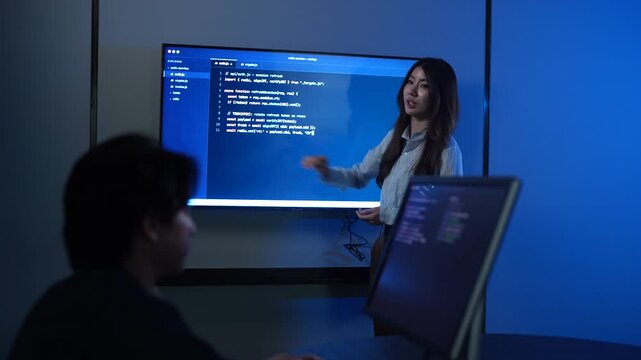 Asian female IT instructor presenting programming code on screens, Smiling tech speaker teaching software development to students, Coding education and corporate technology training seminar concepts
