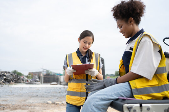 Two female environmental workers review a clipboard and discuss field tasks near a utility vehicle, highlighting teamwork, inspection procedures, safety, and environmental operations.