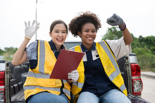Smiling female field worker in reflective safety clothing uses a smartphone beside a utility truck, illustrating digital communication, mobile coordination, outdoor service, and workplace safety.
