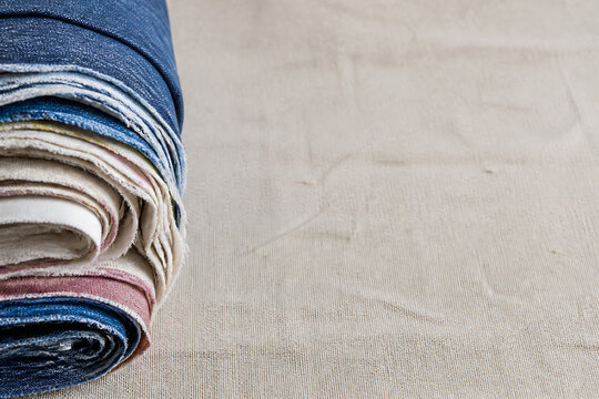 A stack of folded denim and fabric swatches rests on a light beige linen surface.