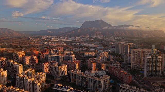 Aerial view of the Benidorm skyline with high-rise apartment buildings and mountains in the background under a golden sunset sky in Benidorm, Valencian Community, Spain.