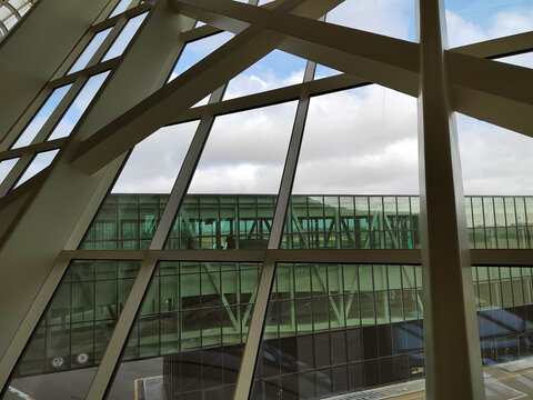 Large diagonal window supports frame a glazed building across an open space, focusing on the interplay of transparency and structural mass