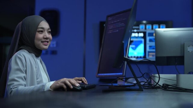 Muslim female developer wearing hijab coding on computer in modern office, Asian professional woman working on software development, Tech industry diversity and corporate programming business concepts