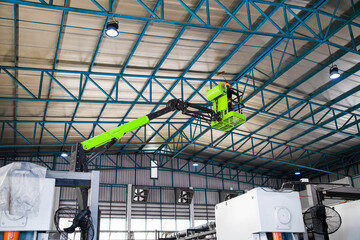 Electric boom lift with worker inside basket elevated to high ceiling for maintenance inside industrial warehouse factory. © Rangsarit