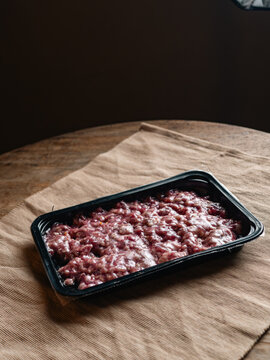 fresh raw minced pork in a black plastic tray wrapped in film on a beige woven fabric surface, uncooked ground meat with white fat ready for cooking, food ingredient