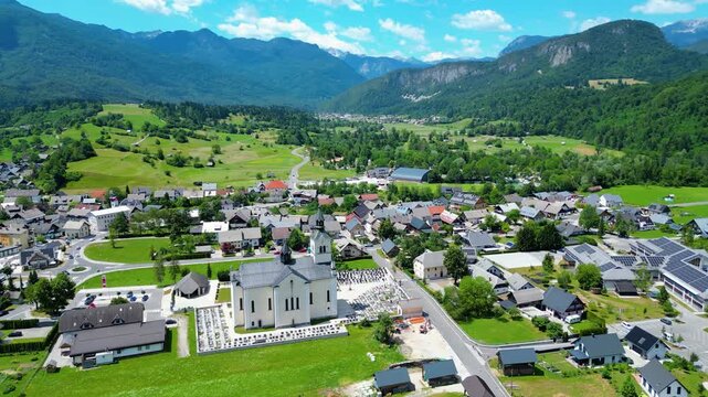 Bohinjska Bistrica, Slovenia, an idyllic village nestled in a lush valley with the Julian Alps as a stunning backdrop. Capturing summer's vibrant beauty from above.