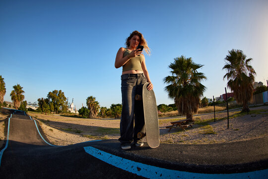 Skater checks phone while standing on ramp in sunny park
