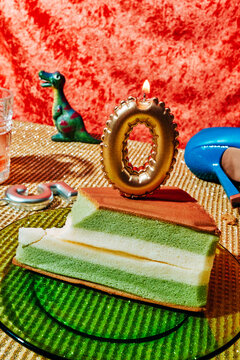 a lit gold zero candle rises above green and cream layer cake