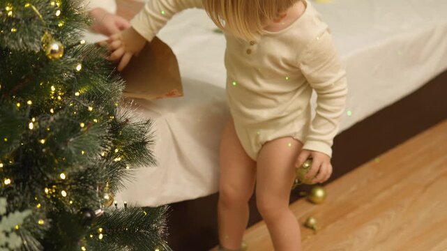 A toddler shares a festive home moment as he walks near a wooden toy train and seasonal decorations. The authentic moment presents active play, toddler development and warm parenting.