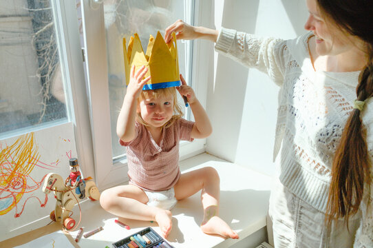 Mother putting a paper crown on her child by the window