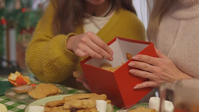 During a cozy Christmas activity, careful hands open a bright red box while organizing edible Christmas gifts. Close product view presents holiday gift preparation with strong commercial appeal.