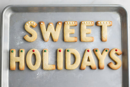 Sweet holidays text made of baked sugar cookies decorated with small colorful candy beads on a metal baking sheet, festive holiday baking theme