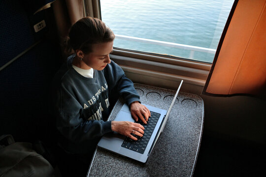 Woman working on laptop in train cabin by window