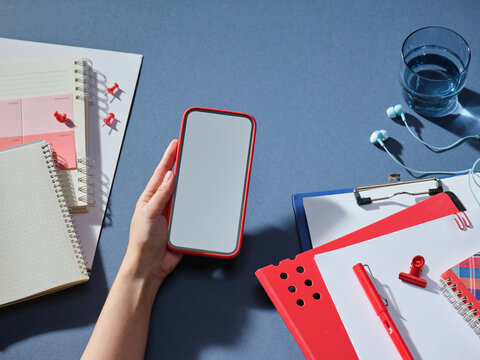 Hand holding smartphone with blank screen surrounded by stationery