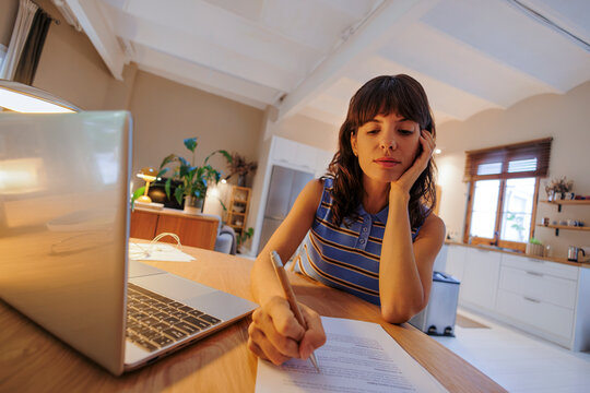 Woman working from home writing on paper at kitchen island