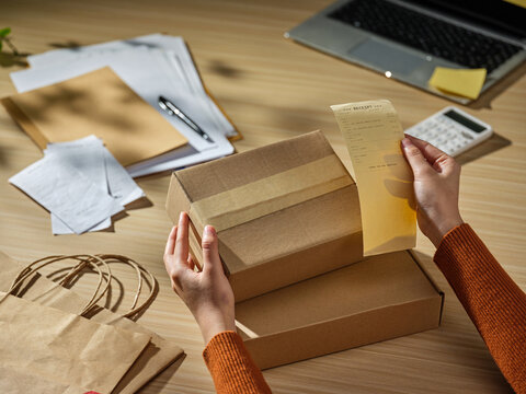 Hands holding a shipping receipt over a cardboard box