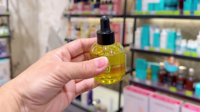 Hand Holding Shampoo Bottle and Hair Care Box in Cosmetics Store &ndash; Hair Oil, Tinted Balm and Conditioner Against Hair Care Shelves