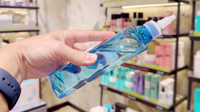 Hand Holding Shampoo Bottle and Hair Care Box in Cosmetics Store &ndash; Hair Oil, Tinted Balm and Conditioner Against Hair Care Shelves