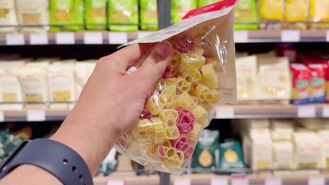 Hand Holding Spaghetti Package in Supermarket &ndash; Choosing Pasta Against Shelves