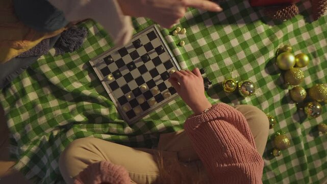 Warm lifestyle footage shows two women who play chess together on a green checkered blanket near the tree. Top-down view conveys screen-free entertainment in a polished lifestyle scene.