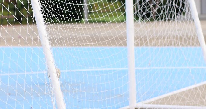 Soccer ball hitting a white goalpost and bouncing away on an outdoor blue sports court, capturing a missed football shot and ball movement, close-up
