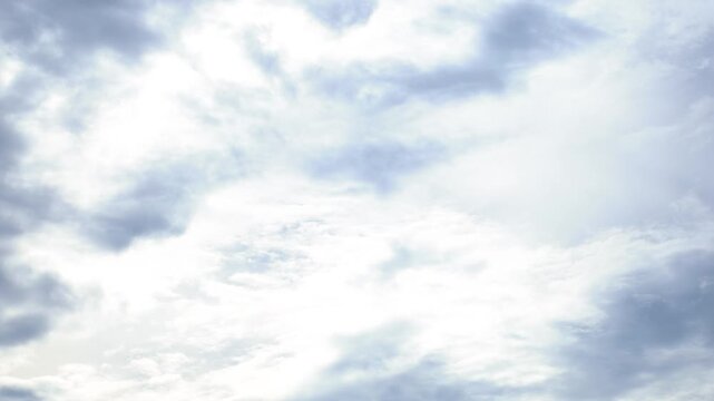 White and light gray clouds moving across a pale blue sky, with diffused sunlight filtering through cloud layers, creating a soft atmospheric background, Timelapse footage