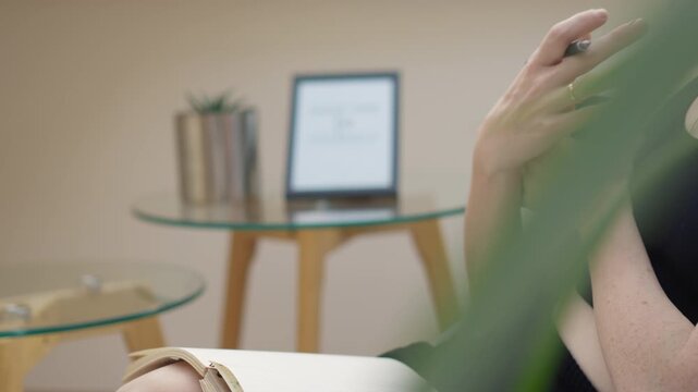 Contemporary office scene featuring a woman in casual attire, focusing on her notes and coffee. Stylish glass furniture and greenery create a calm, productive atmosphere