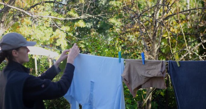 Caucasian woman hanging laundry on a clothesline in a sunny garden. Outdoor air drying, freshness, household routine, and sustainable living. 4K.
