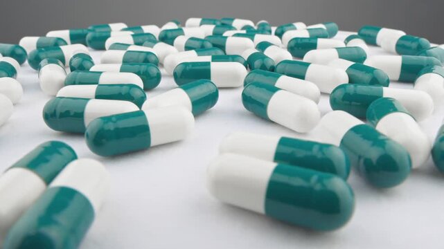 Numerous green and white capsules are spread out on a clean background, representing pharmaceutical advancements. This photo emphasizes health, treatment, and medical innovation