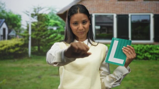 Woman holding learner sign with fist to chest outside a suburban house on street; confidence triumph empowerment.