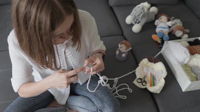 Focused female artist creates crochet toys in a cozy home setting, surrounded by handmade amigurumi dolls and crafting supplies. The scene highlights modern DIY trends and creative hobbies
