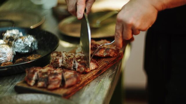 Chef slicing grilled meat on a wooden cutting board in a restaurant kitchen during evening