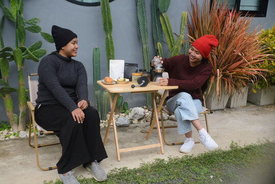 Coffee drip camping friend woman, brewing hot coffee together on foldable wooden table with cactus garden background, during outdoor winter leisure activity in cozy home backyard for lifestyle concept