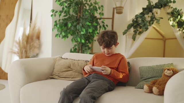 Excited little boy plays video game on cellphone at home, gadget addiction