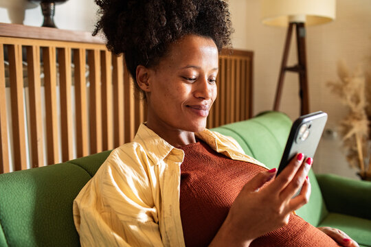 Pregnant woman relaxing on sofa and using smartphone