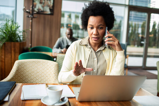 Businesswoman on phone working on laptop in cafe