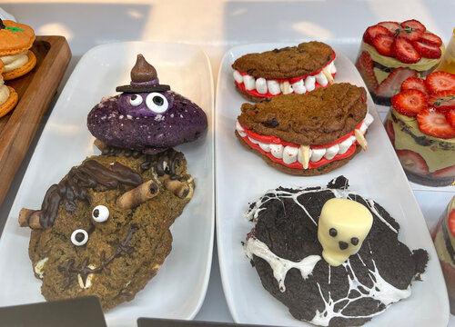 Bakery display showing white plates with large decorated Halloween cookies shaped like witch, vampire teeth, ghost 